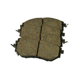 Friction-side view of the full set of four pads, showing brown/tan ceramic-appearance compound with a central vertical slot on each pad and paired stainless retention clips along the sides