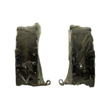 Edge-on view of two shrink-wrapped pads stood on end showing pad thickness profile, wire anti-rattle spring clips visible hooked into underside of each pad