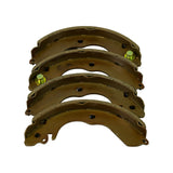 Front-on view of the four shoes lined up, showing yellow zinc-plated steel webs with lightening holes and two shoes fitted with green-tipped self-adjuster pin/spring assemblies