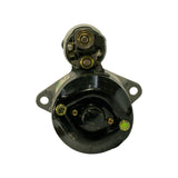Commutator end (rear) face view. Black painted circular end cap with two brass-coloured brush retainer screws and central commutator bore visible. Two-hole flat mounting flange at top. Lucas label partially visible at upper edge.