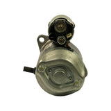 Commutator-end (rear) view of starter motor. Shows brush plate cover with central circular access plug secured by two Phillips screws, two brush holder mounting screws, and ground strap connection point. Solenoid cap visible at top with main terminal stud and trigger terminal.