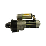 Starter motor opposite side, drive-end at right. Same three-quarter perspective from the other flank. Mounting ear on drive housing visible with bolt holes. Solenoid warning label and tie-wire lead visible top. White spec label on motor body partially visible.