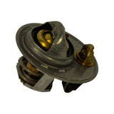 Three-quarter view of the bare thermostat showing the brass jiggle valve, central wax-pellet capsule, secondary spring and faint stamping on the rim