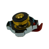 Underside angled view showing the internal sealing assembly. Brass-coloured cylindrical valve body with large black rubber upper seal disc and smaller lower vacuum-relief rubber disc. Coil spring visible around valve stem. Chrome outer ring with lobed tabs for radiator neck engagement.