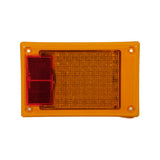 Front face of module, horizontal orientation. Large amber LED lens array occupying approximately two-thirds of face; red retroreflector panel occupying left-hand third. Four white mounting bosses at corners. Lens surface shows minor dust from storage, no damage.