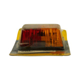 Three-quarter front/left view of blister pack showing dual-colour lens — left half red, right half amber — with ribbed lens face and centre mounting screw. Black base housing visible. Back of card partially visible at edges.