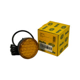 Lamp alongside its Hella retail box. Side-by-side product and packaging shot confirming lamp appearance matches box description. Amber lens and black housing clearly shown. Cable coiled to the left.
