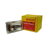 Three-quarter view showing lamp removed from box alongside original packaging. Both box front and lamp lens face visible together. Lamp glass is clear and undamaged. Box shows slight corner crushing.