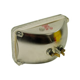 Three-quarter rear view from opposite corner showing second terminal lug side. Stamped markings visible. Glass lens edge shows intact seal all around perimeter. Yellow box partially visible.