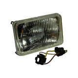 Three-quarter front-right view of the headlight insert showing rectangular profile, mounting tab at top-left corner, and wiring harness with connectors resting below; same lens markings as photo 4 partially visible.