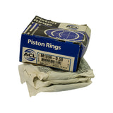 Three-quarter angled view showing front label and top of box, rings still inside in crinkled wax paper. Box corners show light crushing consistent with shelf storage; tape present on one edge seam.