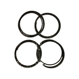 Four individual piston ring packs laid flat, still in clear plastic wrap, arranged in a 2×2 grid. Each pack shows a top compression ring, a second ring, and an oil control assembly. Surfaces appear dark, consistent with phosphate or nitrided coating.