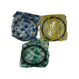 Three piston ring packets laid flat from above: 1st Ring (blue RIK tissue, two compression rings), 2nd Ring (yellow RIK tissue, two compression rings), and Oil Ring (green RIK tissue, two oil control rings). All individually wrapped in original factory tissue, unfitted.