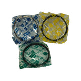 Same three piston ring packets from slightly different angle, confirming all are still sealed in original tissue with no visible damage or distortion to rings. Blue = 1st Ring, yellow = 2nd Ring, green = Oil Ring.