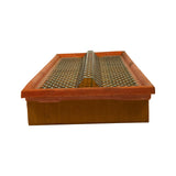 Short-end profile view showing depth of the filter element; orange rubber gasket frame visible on top edge, pleated paper visible along the sides, and a raised metal spine running along the centre of the mesh face.