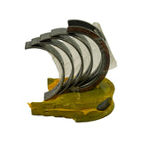 Bearing set fan-out, front-quarter view. Five or more half-shell bearing shells interleaved with protective plastic wrapping still on some shells. Yellow plastic tray visible at base. Tri-metal layered construction clearly visible on shell edges.