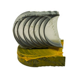 Angled three-quarter view of bearing stacks showing the polished inner surface of upper shells and dark tri-metal back, with yellow-coated lower shells beneath. Multiple oil groove channels visible across the inner face of upper shells.