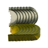 Top-down view of both bearing shell stacks fanned out — upper halves (dark grey tri-metal face) in one stack, lower halves (yellow coating, broad semi-circular profile with locating lug notch) in second stack. All shells appear factory-fresh.